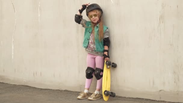 Весела маленька дівчинка стоїть з жовтими ковзанами в руках і посміхається — стокове відео