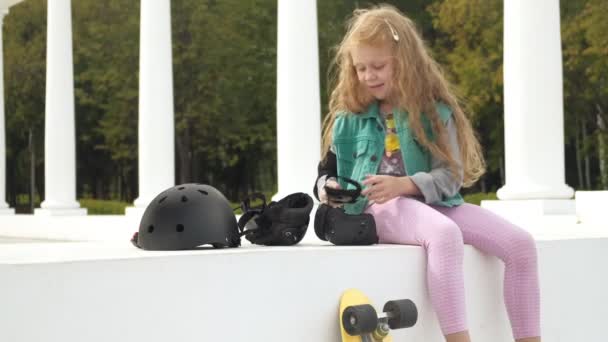 Little girl dresses protection: helmet, knee pads and elbow pads. Sunset — Stock Video