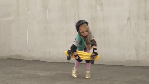 Een vrolijk klein meisje staat met een gele Skate in haar handen en glimlacht — Stockvideo