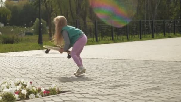 Une petite fille monte sur une planche à roulettes jaune — Video