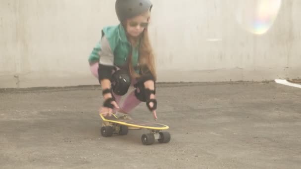 En liten flicka rider på en gul skateboard — Stockvideo