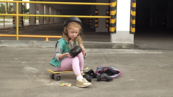 La petite fille s'habille de protection : casque, genouillères et coudières. Coucher de soleil — Video