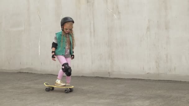 Маленькая девочка едет на жёлтом скейтборде — стоковое видео