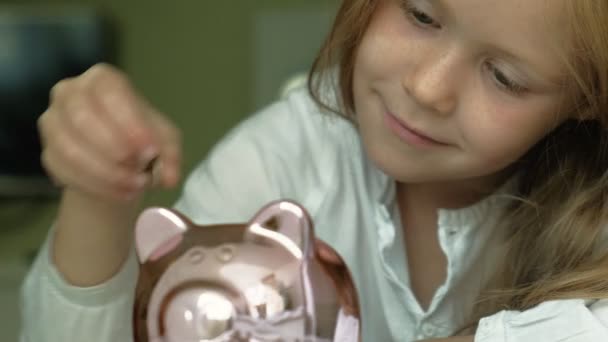 Girl preschooler puts money in a piggy bank pink pig — Stock Video