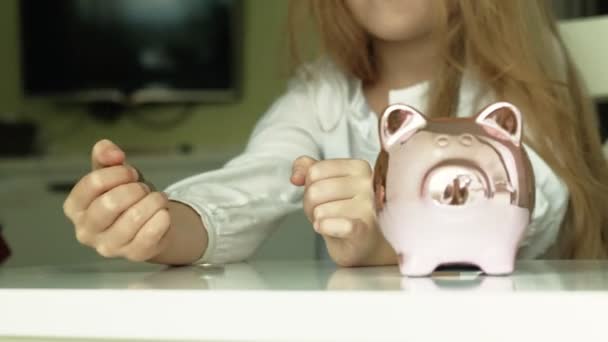 Девочка-дошкольница кладет деньги в копилку розовой свиньи — стоковое видео