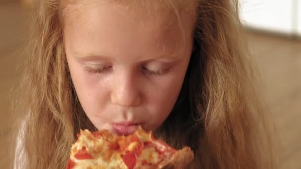 Prechooler girl eating pizza while sitting on floor in room — стоковое видео