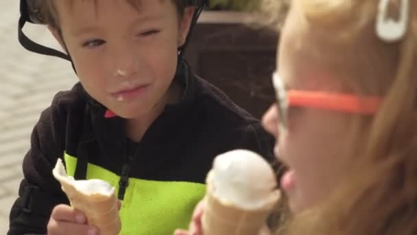 Un niño y una niña están sentados en un banco del parque y comiendo helado. Verano — Vídeos de Stock