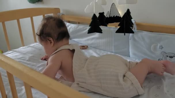 Toddler dziewczyna uczy się trzymać głowę leżącą w łóżeczku. — Wideo stockowe