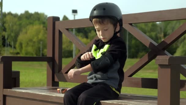Ein Vorschulkind sitzt auf einer Bank im Park und legt Schutz auf Kopf, Knie und Arme. Sommer — Stockvideo