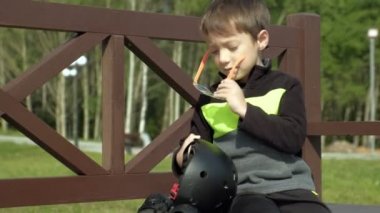 Bir okul öncesi çocuk parkta bir bankta oturur ve başını, dizlerini ve kollarını koruma koyar. Yaz