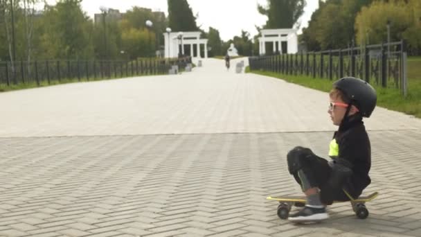 Um menino pré-escolar com um capacete de proteção monta um skate em Park. Verão — Vídeo de Stock