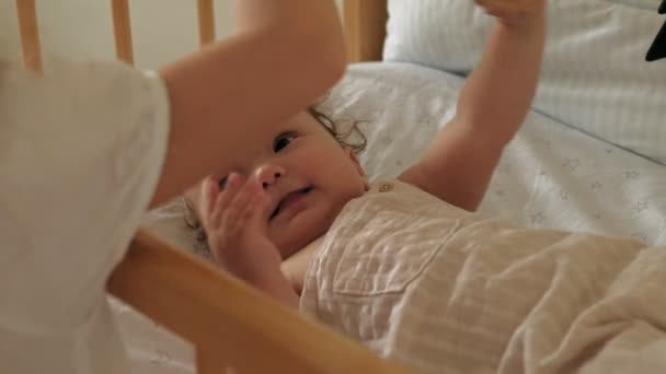 Vorschulmädchen steht mit Kind an der Krippe, beruhigt sie. Pflege einer kleinen Schwester — Stockvideo