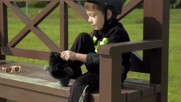 A preschooler fiú ül egy padon a parkban, és teszi a védelem a fejét, térdét és karját. Nyári — Stock videók