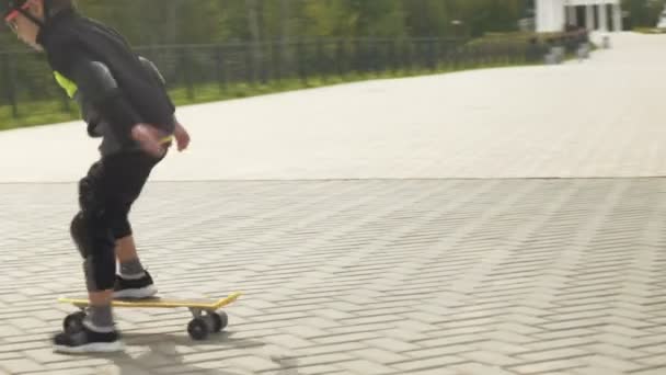 Un bambino in età prescolare con un casco protettivo cavalca uno skateboard a Park. Estate — Video Stock