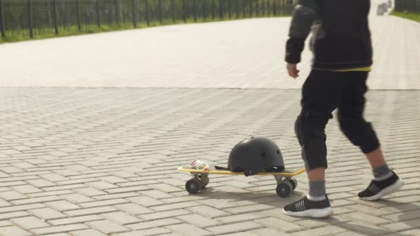 보호 헬멧을 쓴 미취학 아동 소년이 공원에서 스케이트보드를 탄다. 여름 — 비디오