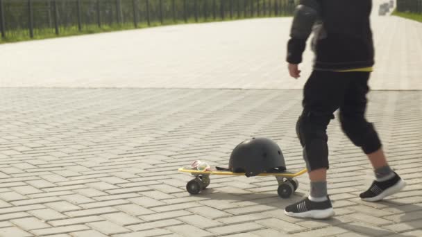 Un bambino in età prescolare con un casco protettivo cavalca uno skateboard a Park. Estate — Video Stock