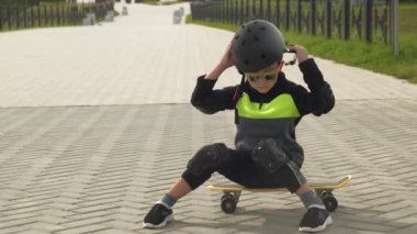 Koruyucu kasklı bir okul öncesi çocuk Park'ta kaykay sürüyor. Yaz