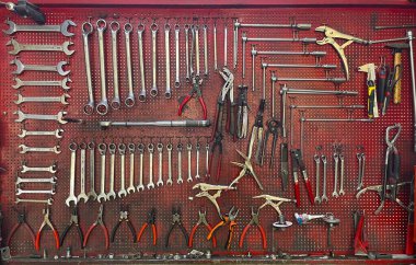 Atölyede anahtarlar, pense, kıskaçlar, çekiçler ve tornavidalarla dolu düzenli bir alet duvarı var. Tamir ekipmanları ve garaj detaylarının endüstriyel geçmişi.