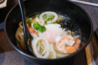 Udon 'un deniz ürünleri mürekkep balığı, karides ve yumurtayla yakın çekimi. Japon mutfağı. Yiyecek ve içecek konsepti. Gıda arkaplanı.