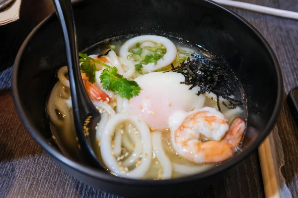 Udon 'un deniz ürünleri mürekkep balığı, karides ve yumurtayla yakın çekimi. Japon mutfağı. Yiyecek ve içecek konsepti. Gıda arkaplanı.