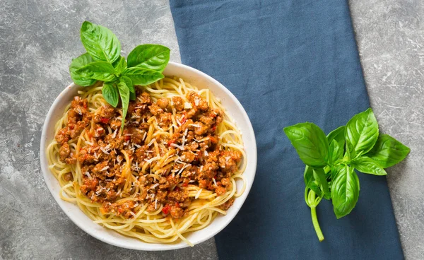 Bolonez soslu spagetti, rendelenmiş parmesan ve gri arka planda bir tutam fesleğen. Üst görünüm