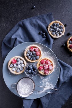 Büyük gri bir tabakta taze yaban mersini ve ahududu ile lezzetli bir tatlı. Siyah arka plan. en üstteki görünüm
