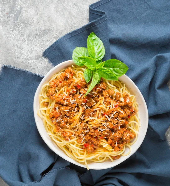 Bolonez soslu spagetti, rendelenmiş parmesan ve gri arka planda bir tutam fesleğen. Üst görünüm