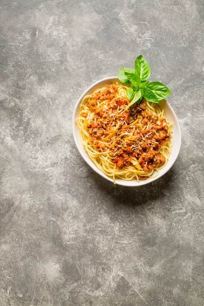 Bolonez soslu spagetti, rendelenmiş parmesan ve gri arka planda bir tutam fesleğen. Üst görünüm, boşluk kopyala