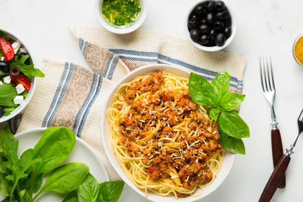Yemek masası konsepti. Bolonez soslu spagetti, sebze ve zeytinli yeşil salata, parmesan peyniri ve baharat. Üst görünüm