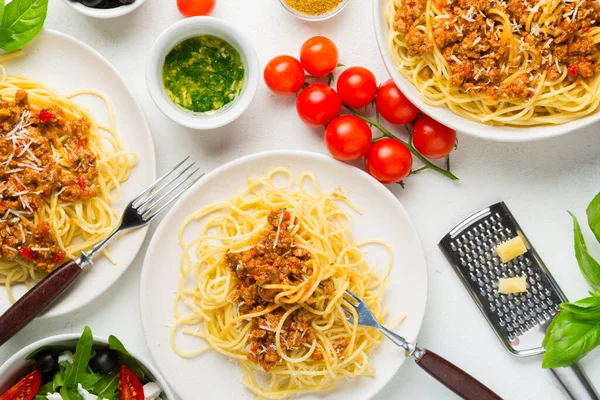 Yemek masası konsepti. Bolonez soslu spagetti, sebze ve zeytinli yeşil salata, parmesan peyniri ve baharat. Üst görünüm