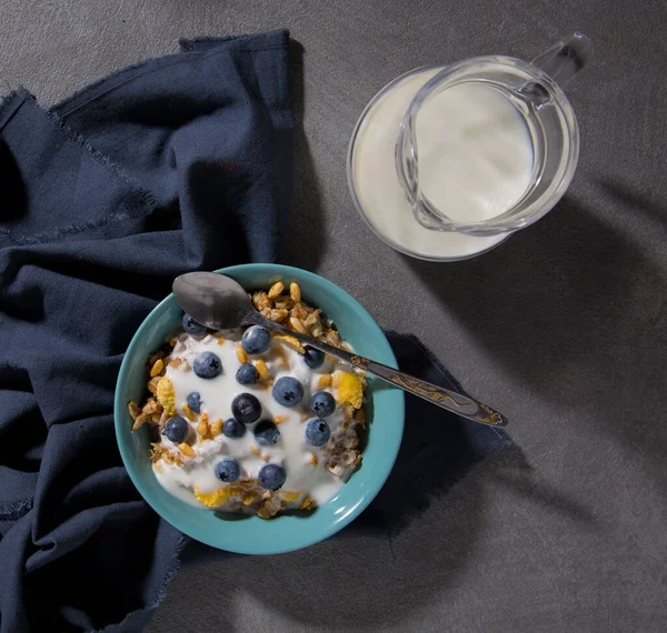 Bir kase granola ve gri arka planda bir sürahi süt. Üst görünüm