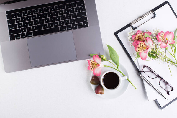 Workspace with laptop, notepad, tablet, glasses, cup of black coffee and a peruvian lily flower on a white background. Top view
