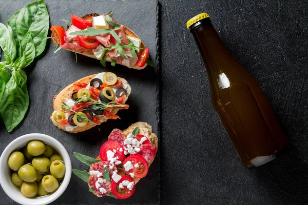 Geleneksel Hughchetta. Jamonlu İtalyan antipasti seti, guanchial sosis, zeytin, süzme peynir, roka ve siyah arkaplanda domates. Üst görünüm