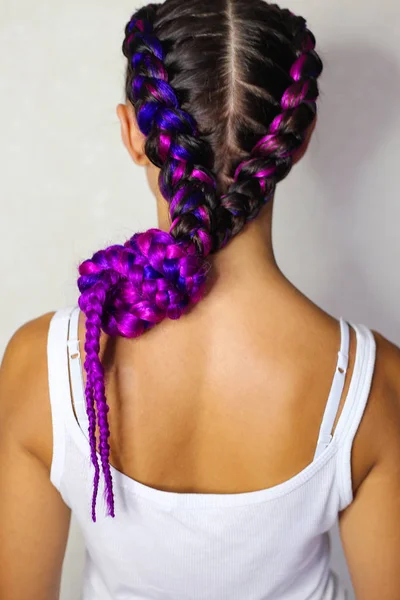 这个女孩编织着两条带紫色和粉红色 Artific 的辫子 — 图库照片