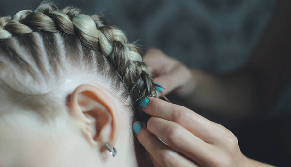 the process of braiding boxer braids on the girls head, the master makes her hair in a beauty salon, hands close-up