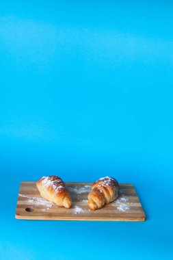 Ahşap masa üzerinde mavi arka planı olan kruvasanlar. Seçici odaklanma. Dikey sürüm.