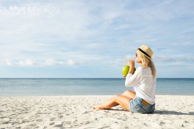 Kumsalda oturan ve taze hindistan cevizi suyu içen bir kadın. Tropikal konseptte tatil ve yaz tatili. 