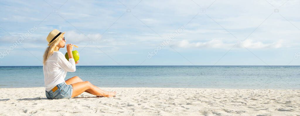Woman sitting on the beach and drinking fresh coconut juice.	Vacation in tropical concept. Banner and panoramic edition.