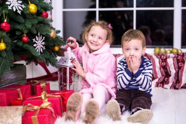 İki küçük çocuk, kardeşi ve kız kardeşi, Noel iç ve hediyeler arka plan üzerinde oturuyor. Mutlu Noeller ve mutlu tatiller! Noel ağacı kapalı.