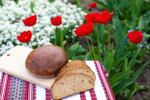 Pane di segale su una tavola di legno sullo sfondo di fiori primaverili. pane fresco su uno sfondo di tulipani fioriti — Foto Stock