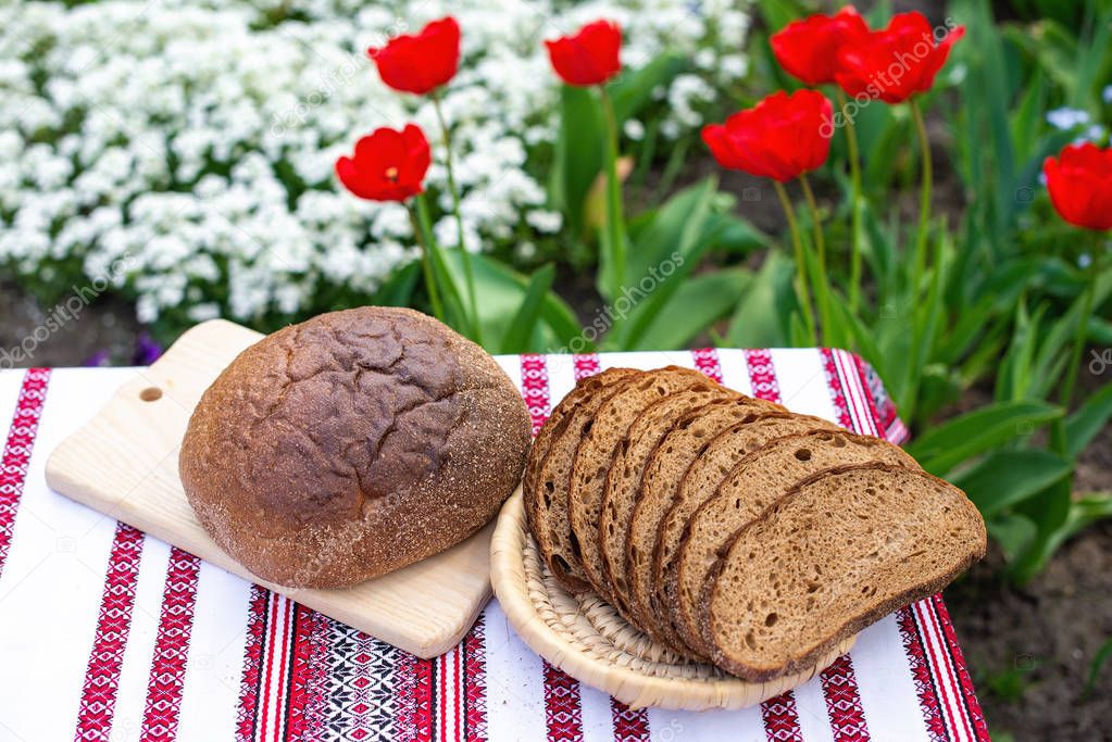 Rye bread on a wooden board against the background of spring flowers. fresh bread on a background of blooming tulips