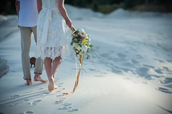 Amantes caminan sobre la arena con un ramo de swetow —  Fotos de Stock