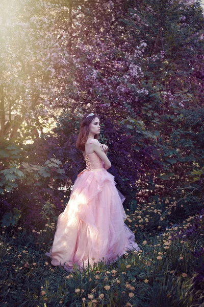 Flicka i en rosa klänning i en blomsterträdgård — Stockfoto