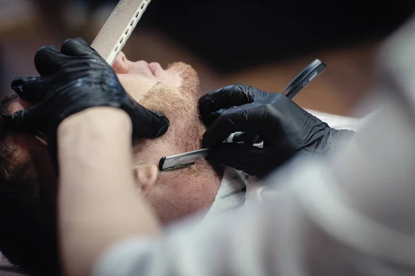 戴着黑色手套的理发师把客户的剃须刀胡子剃光了 — 图库照片
