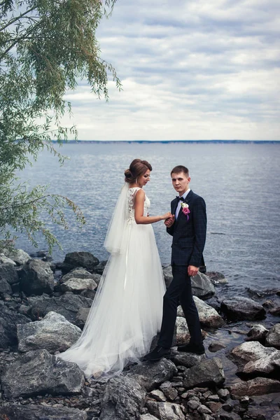 Um par de jovens recém-casados nas pedras junto ao grande rio — Fotografia de Stock