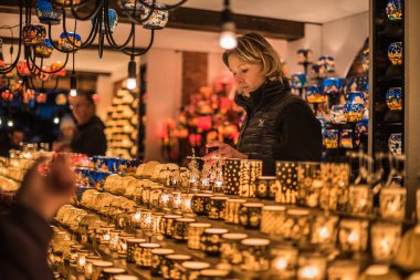 Vienna, Austria - December 24, 2017. Lighting colorful glass candle holders in kiosk at Viennese Christmas market. Close view of Xmas fair stall with seller selling craft souvenirs and candelabras. clipart