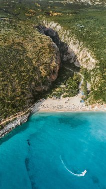 Arnavutluk 'taki Gjipe Sahili ve kanyonunun insansız hava aracı görüntüsü. İyon Denizi 'nin turkuaz sularında yelken açan beyaz tekne, şemsiyeli kumlu plaj ve yaz boyunca kum üzerinde dinlenen insanlar..