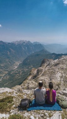 Dağların tepesinde oturan iki yürüyüşçü, tırmanıştan sonra dağlık araziyi gözlemliyor. Erkek ve kadın dağların tepesinde, turist sırt çantaları yakınlarda dinleniyor. Macera dağ yolculuğu konsepti.