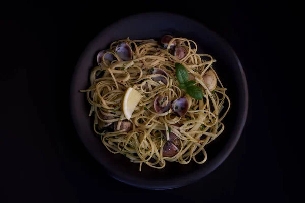 Spagetti vongole, istiridye ve midye ile İtalyan deniz ürünleri makarna, otlar siyah arka plan ile plaka. Geleneksel İtalyan deniz mutfağı, yakın çekim, en iyi manzara. Kopyalama alanı