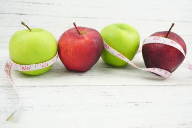 Ahşap arka plan üzerinde ölçüm bandı ile Yeşil ve Kırmızı Elmalar.